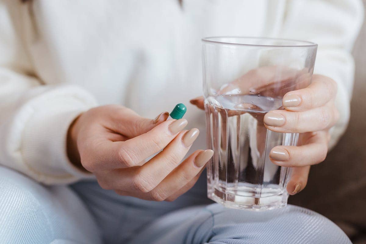 Person holding a green capsule in one hand and a glass of water in the other, preparing to take medication.